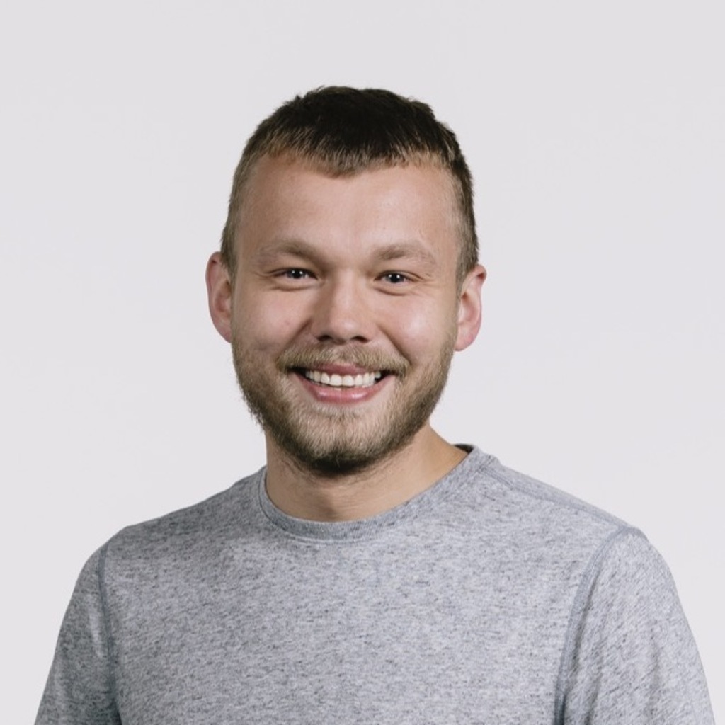 Wojciech Zaremba smiling in a grey t-shirt on a grey background.
